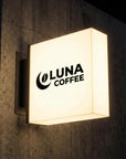 Illuminated wall mounted coffee shop sign featuring modern branding on brick wall