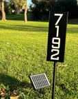 Illuminated house numbers on metal stake glowing brightly at night