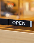 Black Open / Closed slider sign on a wooden café door with OPEN showing