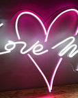 Neon sign with heart and 'Love Me' text on a dark background
