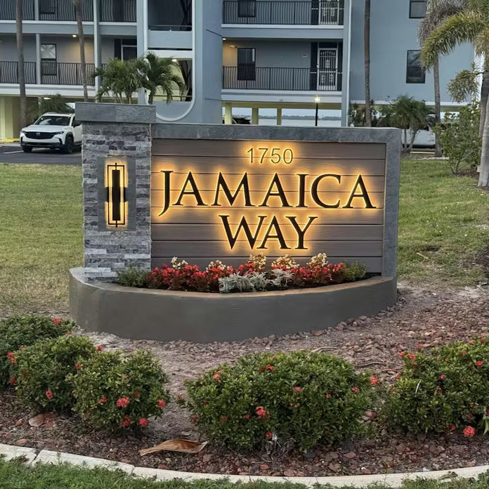 Luxury community entrance sign featuring backlit gold lettering and address numbers on a large stone monument.