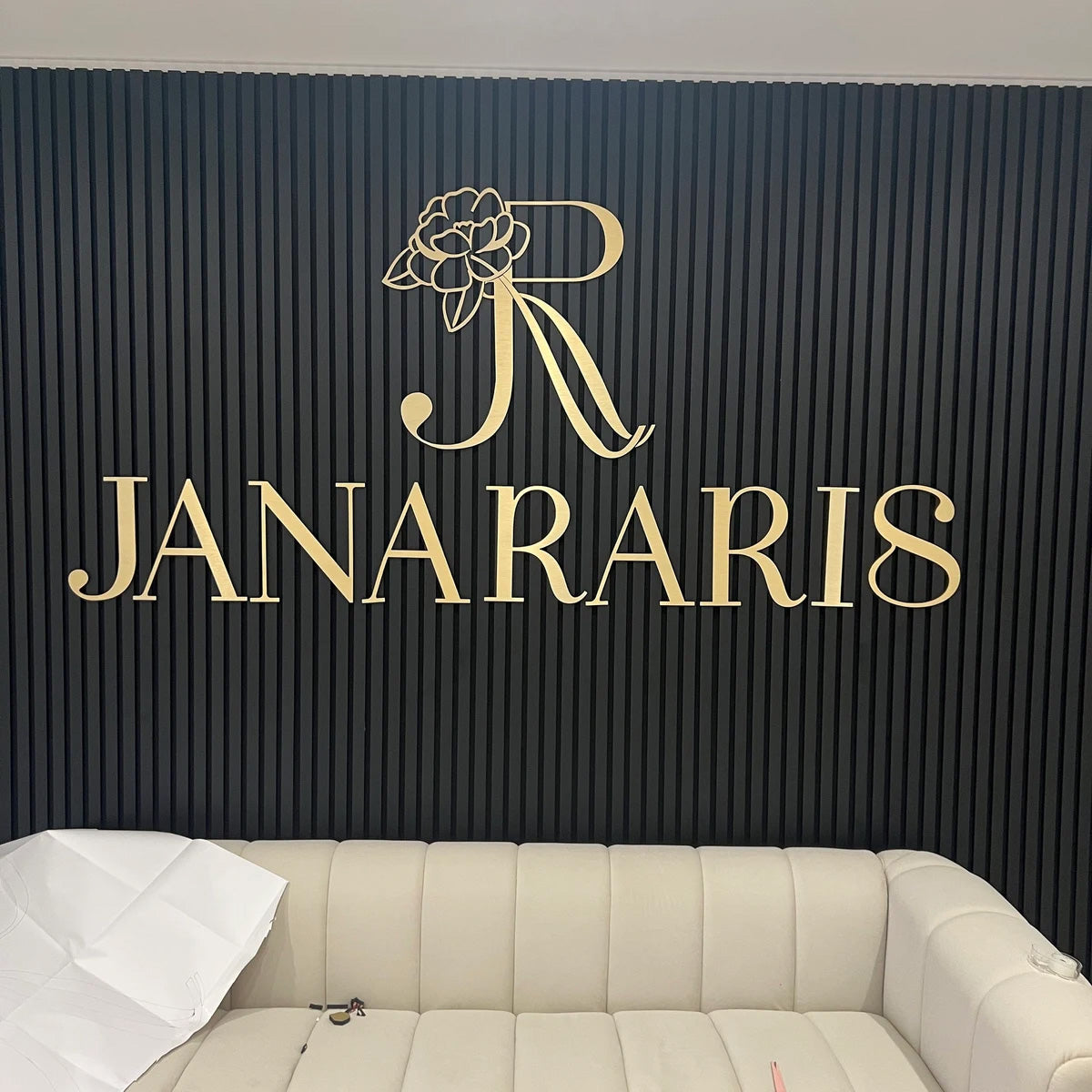 Custom gold 3D dimensional lettering with a delicate floral icon mounted on a modern black vertical-slat interior wall