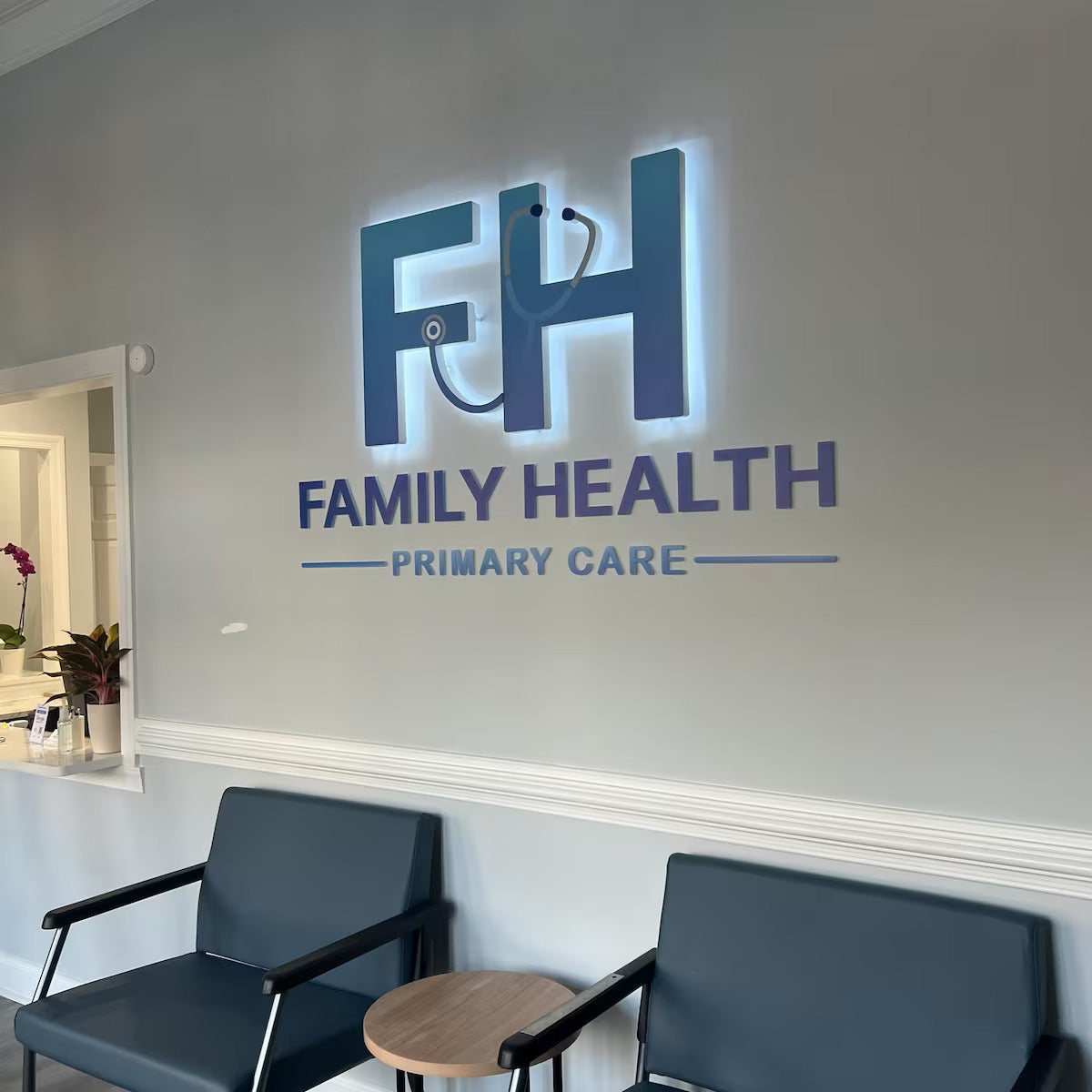 Custom 3D illuminated medical clinic lobby sign with blue backlighting mounted on a light gray interior wall.