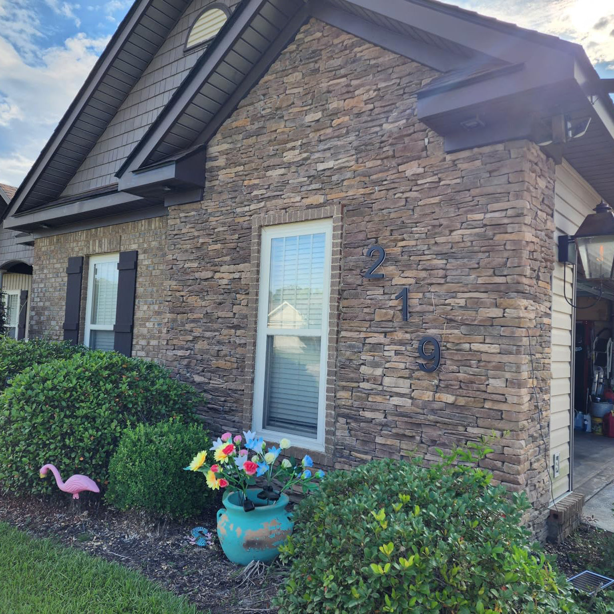 Close-up of a residential stone exterior wall featuring large blue house numbers '21' integrated with traditional home landscaping and garden decor.