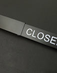 Black door handle with 'CLOSED' label on a black background