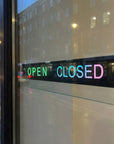 Neon open and closed sign on a glass door with city street reflection.