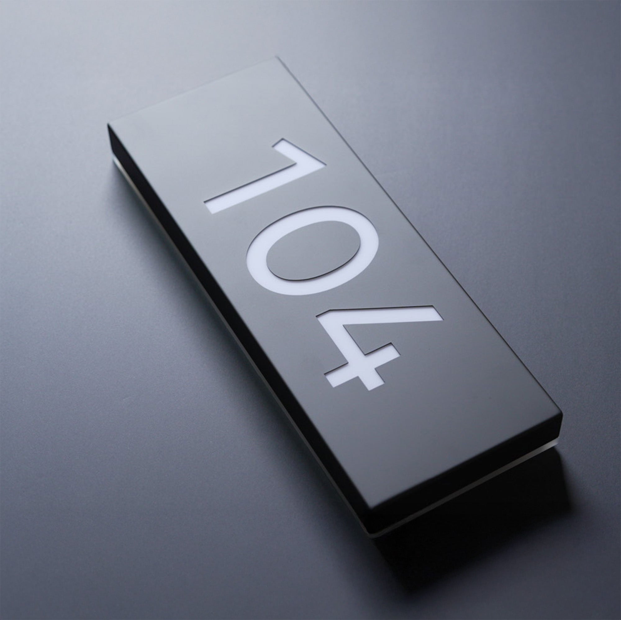 Metallic door plaque with the number '104' on a reflective surface