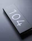 Metallic door plaque with the number '104' on a reflective surface