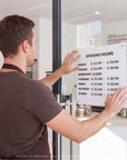 OPENING HOURS' onto a glass door in a bright, modern cafe or restaurant.