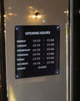 Opening hours sign on a door with a bar interior in the background