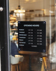 Opening hours sign on a glass door with a blurred interior background