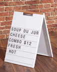 White A-frame menu board with a wood handle displaying a daily special menu against a brick wall