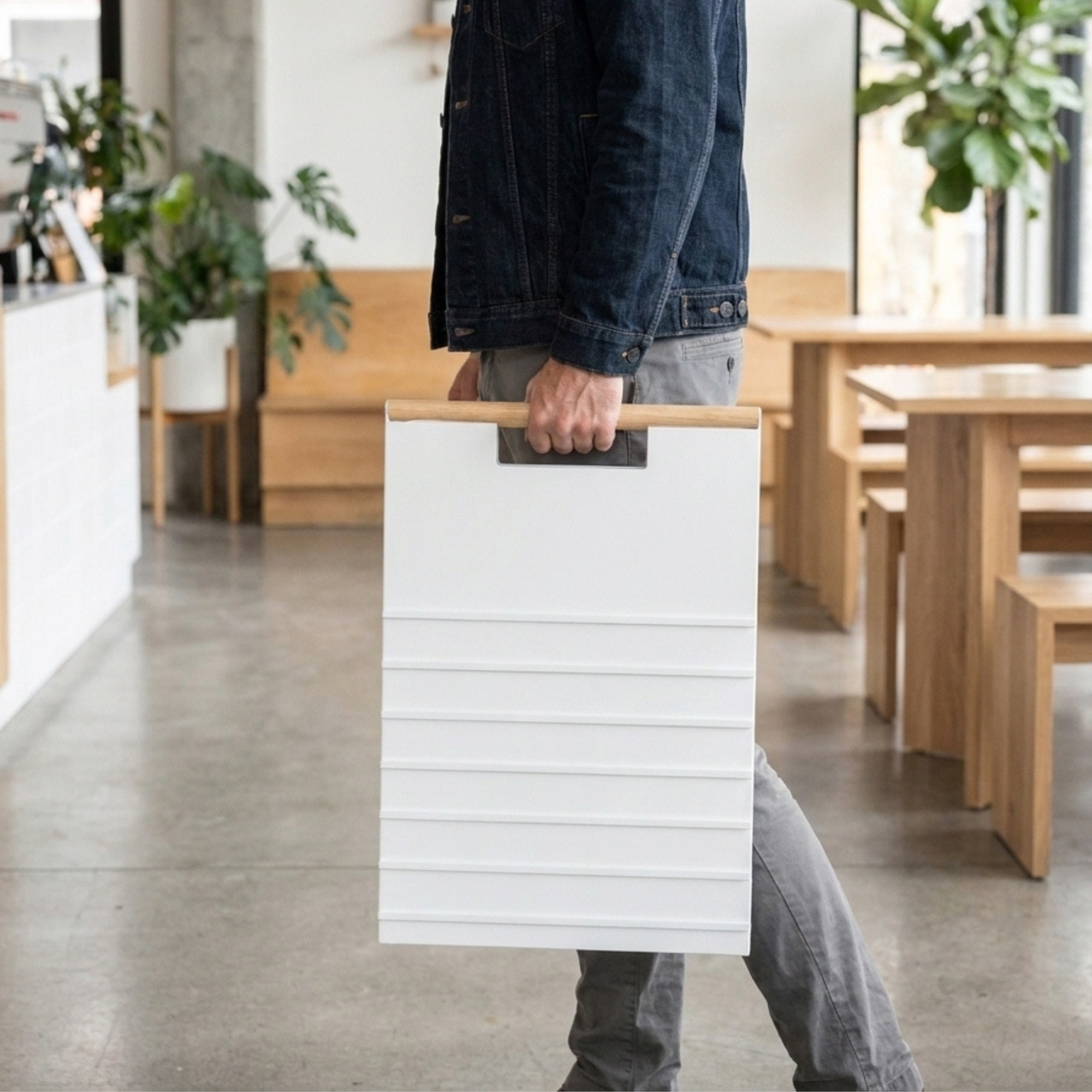 Person carrying a folded white A-frame menu board one-handed by its wood handle rail through a cafe