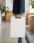 Person carrying a folded white A-frame menu board one-handed by its wood handle rail through a cafe