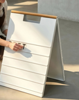 Barista sliding a black letter tile into the rail of a white A-frame menu board with a wood handle