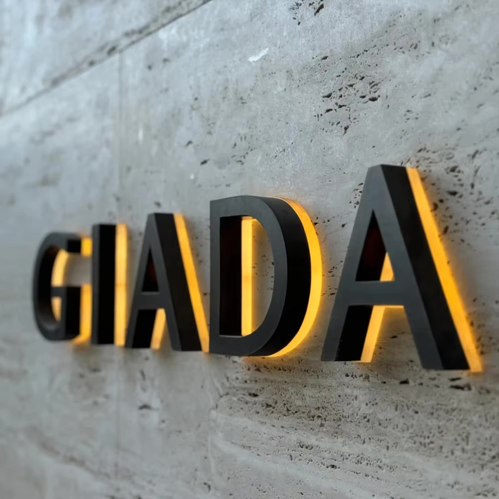 Custom black metal backlit channel letters "GIADA" mounted on a concrete wall with warm halo lighting.