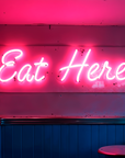 Pink Eat Here circular neon sign for retro restaurant dining area