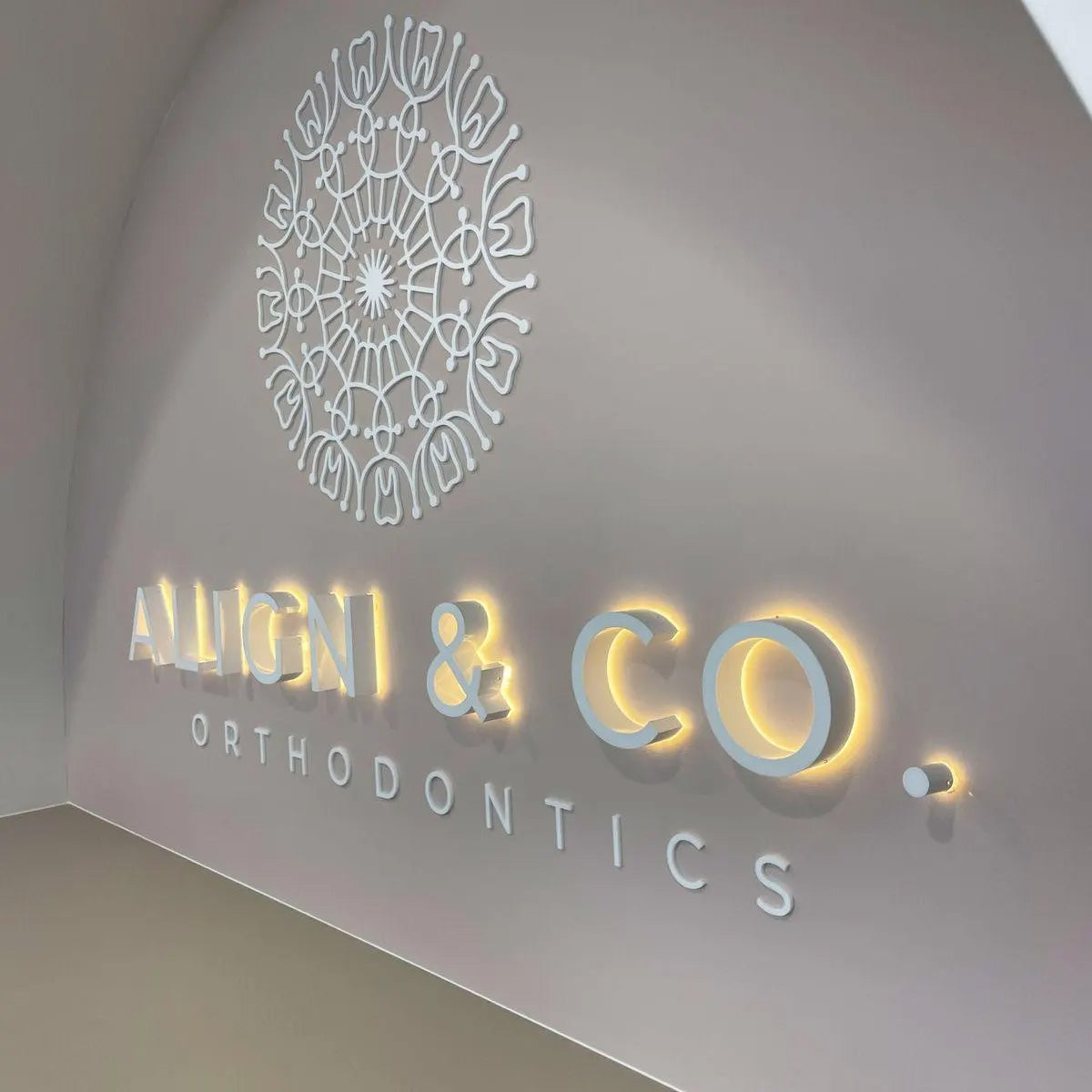 Circular gold halo-lit dental office logo with an intricate geometric pattern on a textured white wall.