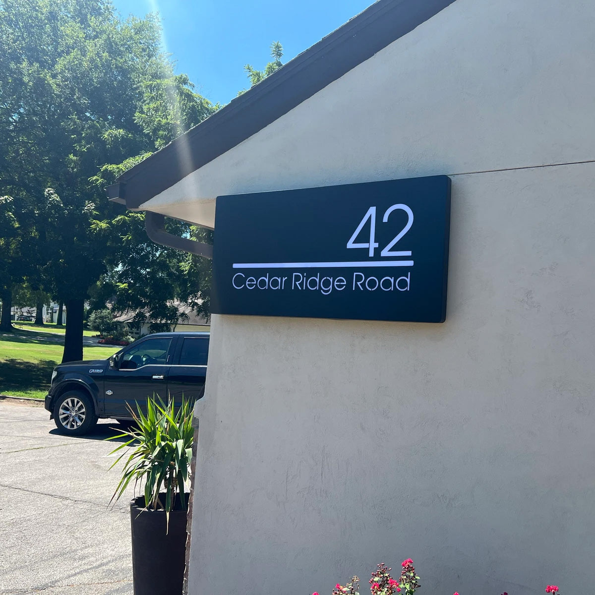 Modern residential address sign with large white illuminated numbers and street name mounted on a clean white pillar at dusk