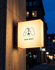 Illuminated outdoor square sign hanging on wall at night with warm lighting