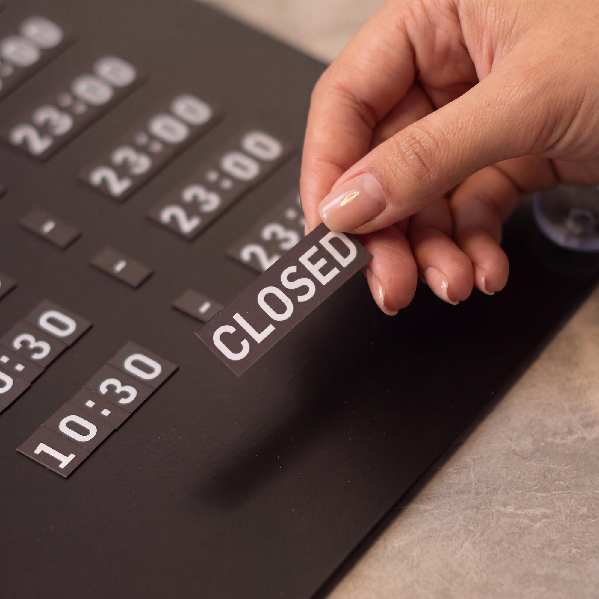 Hand swapping a CLOSED tile on the black magnetic business hours sign