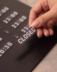 Hand swapping a CLOSED tile on the black magnetic business hours sign