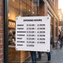 White magnetic business hours sign mounted on a cafe glass door with weekly opening hours set in changeable tiles