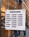 White magnetic business hours sign mounted on a cafe glass door with weekly opening hours set in changeable tiles