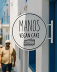 Manos Vegan Cake sign on a building with people walking in the background