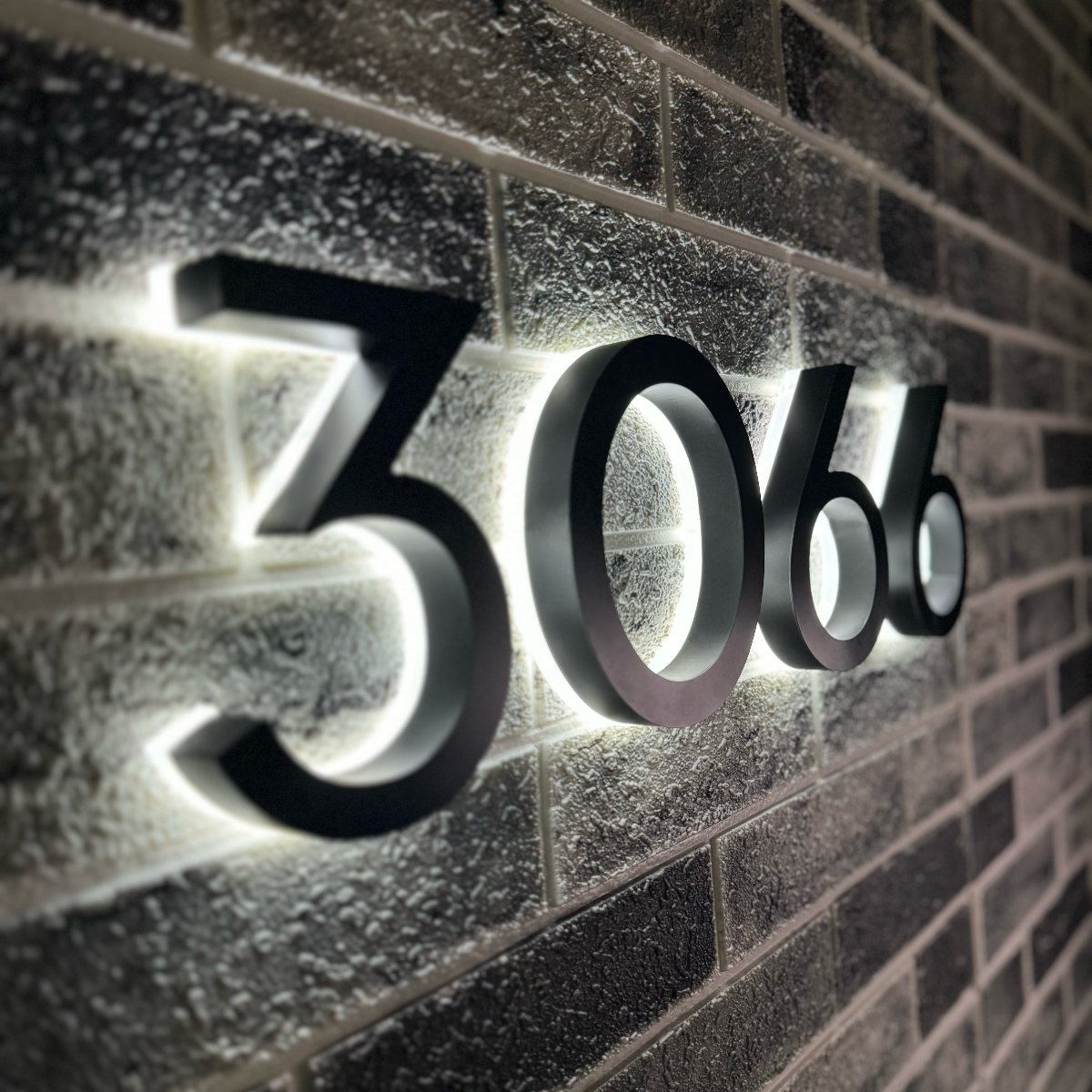 Modern backlit house numbers 3066 mounted on dark stone wall for high contrast visibility