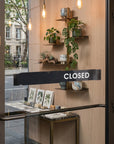 Storefront with 'CLOSED' sign on glass door, shelves with plants and decor.