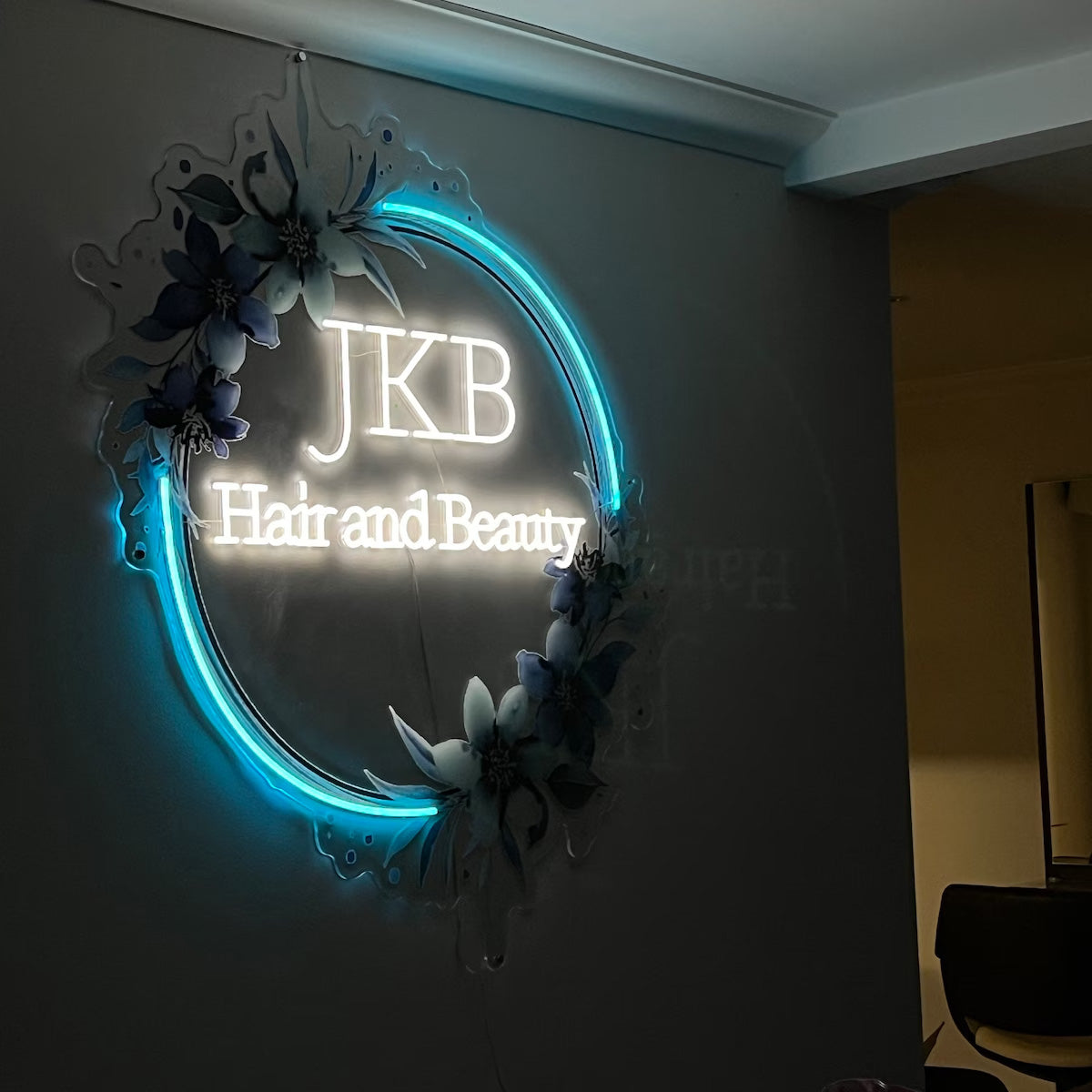 Luxury teal circular halo backlit sign surrounded by a matching floral arrangement on a dark interior wall.