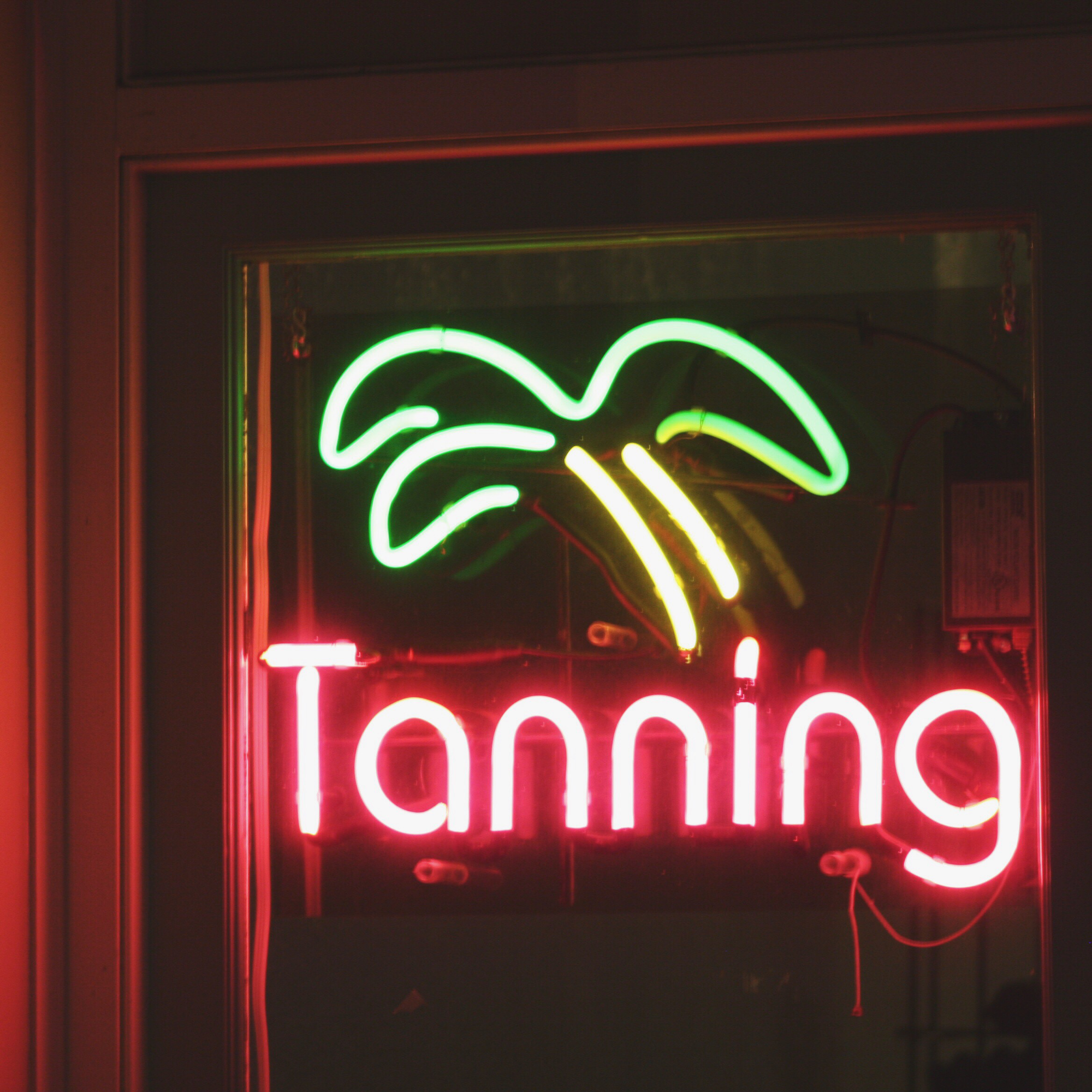 Tanning salon neon window sign featuring green palm tree design