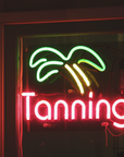 Tanning salon neon window sign featuring green palm tree design